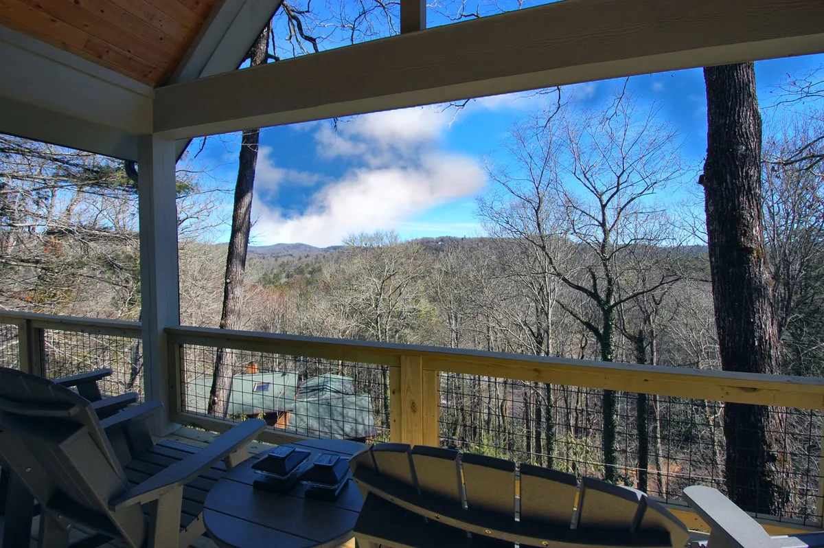 The image showcases an inviting outdoor seating area surrounded by lush trees, overlooking sweeping mountain views. The scene is tranquil, with misty morning fog rolling over the peaks, hinting at the peaceful seclusion and natural beauty that define the property. The space invites relaxation, whether enjoying a coffee at sunrise or stargazing at night.