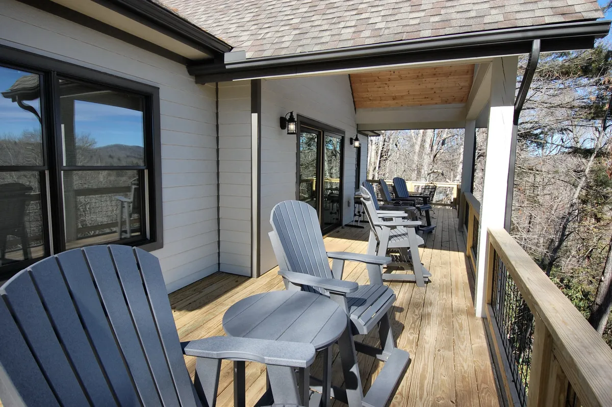 This image features a wooden deck outfitted with classic Adirondack chairs, facing a breathtaking mountain view. The calm setting emphasizes the outdoor living space and the inviting atmosphere for both sunrise and sunset moments.