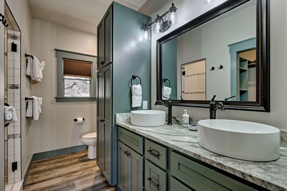 A modern bathroom featuring double sinks with sleek basins, a large mirror, stylish lighting fixtures, and a spacious shower area. The design is both functional and elegant, perfect for morning routines or unwinding with a relaxing bath.