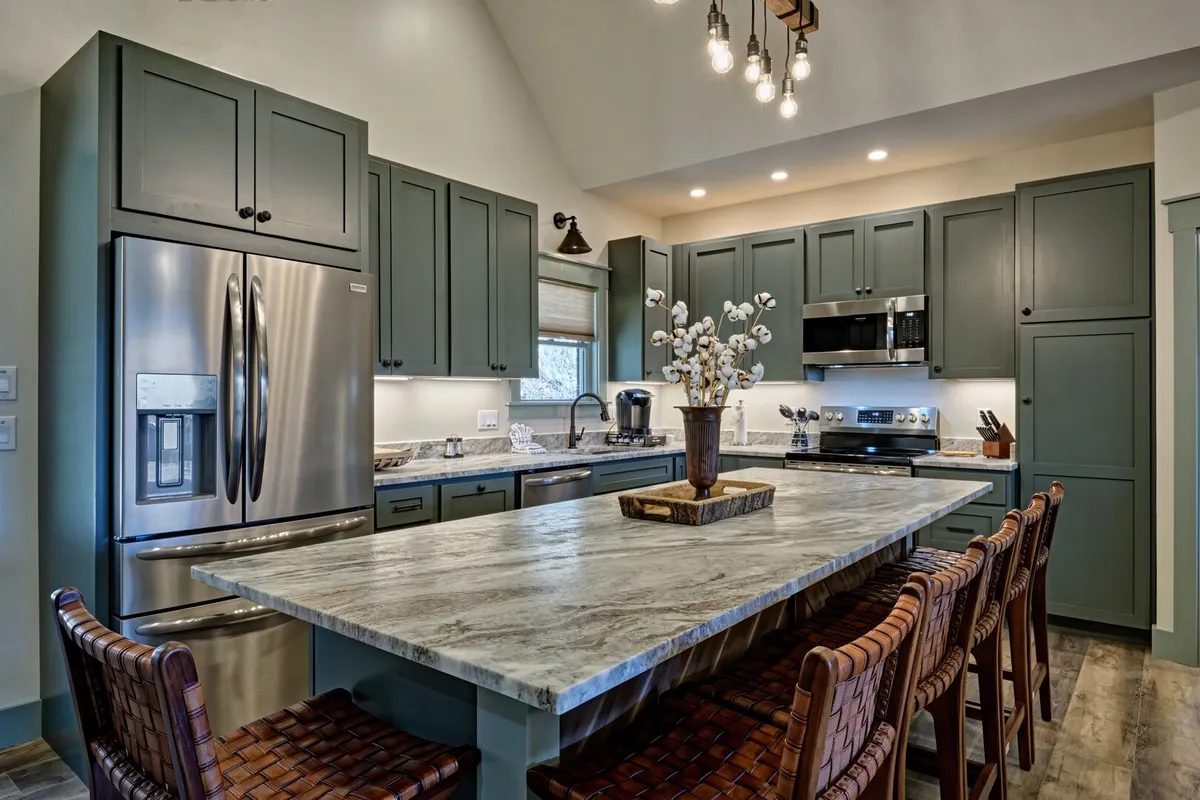 A closer perspective of the kitchen emphasizes the large, modern kitchen island, sleek appliances, textured cabinetry, and a decorative vase. The space feels contemporary and ideal for both casual dining and special occasions.