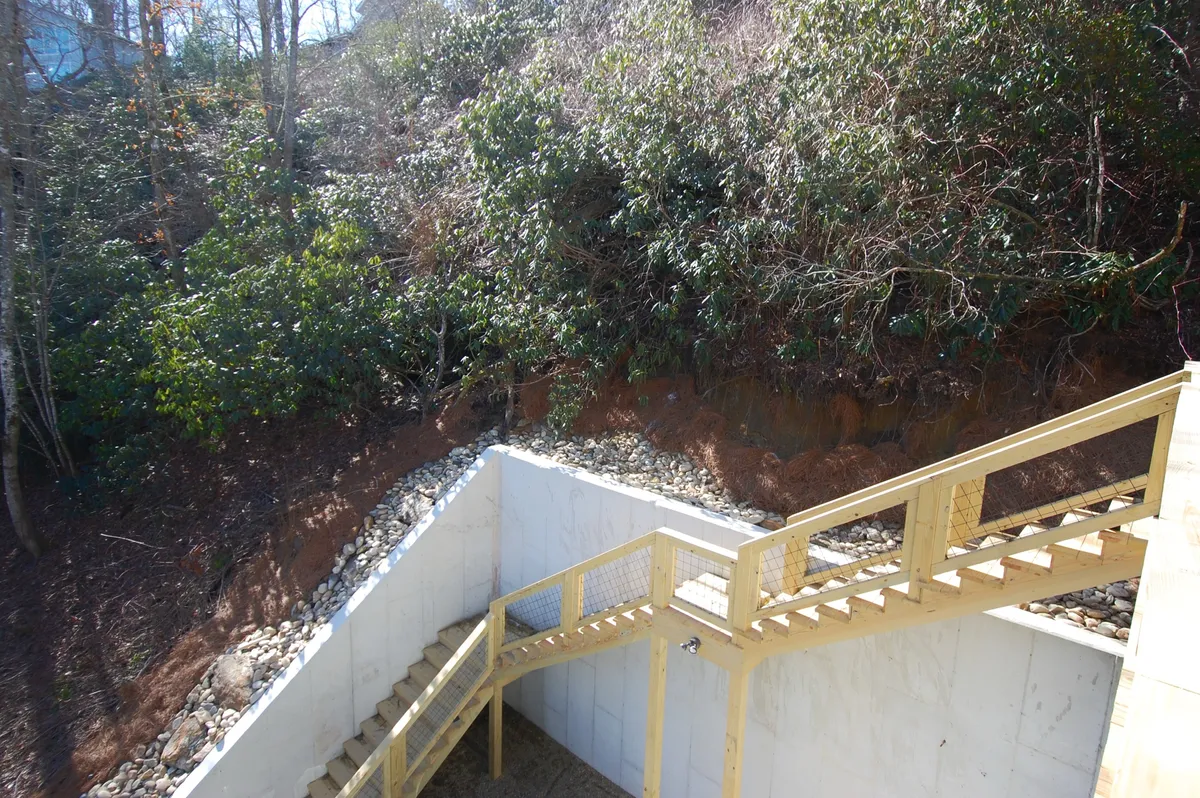 A wooden staircase set amid lush greenery, with a rocky base that hints at the natural elevation and terrain surrounding the property. The scene captures an inviting path leading outdoors, evoking the spirit of adventure and exploration that characterizes the Highlands area.