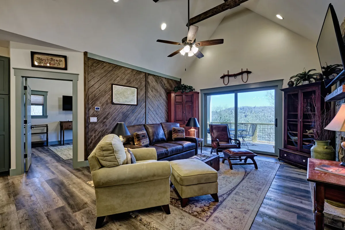 A bright, inviting living area with a comfortable sofa, coffee table, and a window offering serene views of the outdoors. Decor elements such as shelves and artwork add warmth, while the window view subtly hints at the property’s beautiful natural setting.