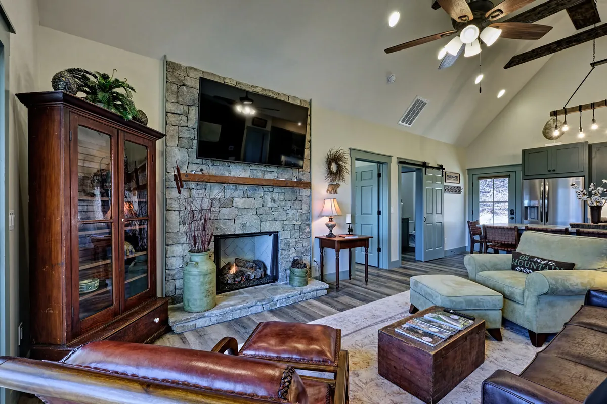 A warmly lit living room with a comfortable sofa, a stone fireplace, and a coffee table. The windows suggest a cozy space that could be used for relaxing after a day of exploring the town with your dog, and the overall atmosphere is welcoming and homey.