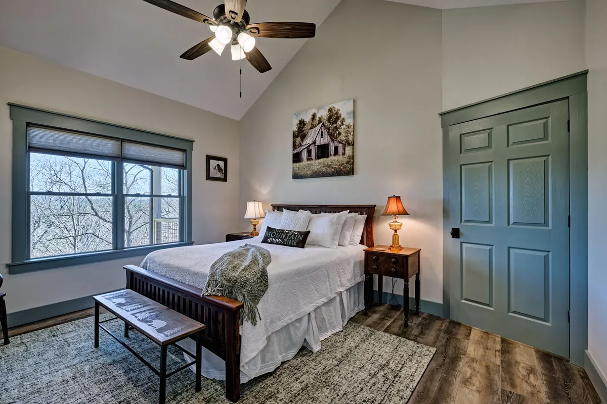A cozy bedroom showcasing a comfortable bed positioned beside a window, with soft light filtering in. The room features a nightstand, charming artwork, and a plush rug, creating a serene and inviting atmosphere ideal for unwinding after a day of adventure.