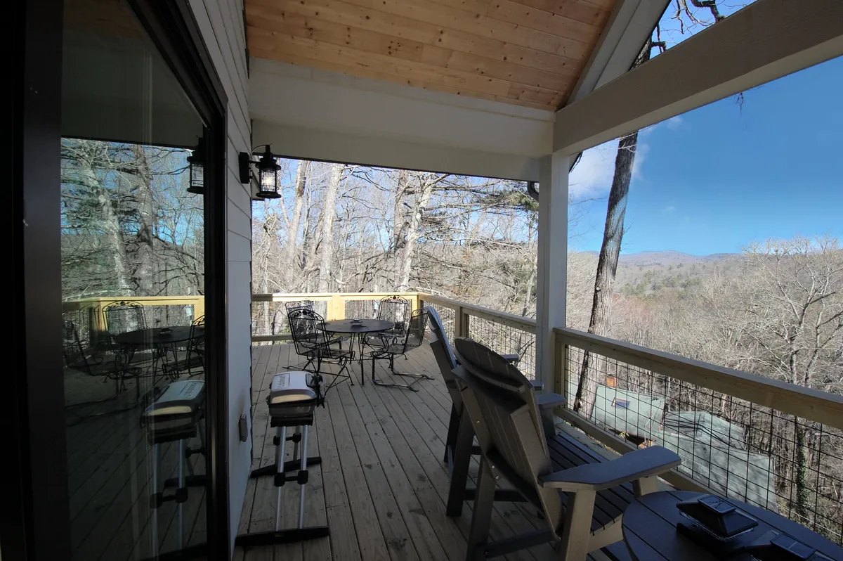 A stylish wooden deck with comfortable furniture, a glass railing, and a sweeping view of the mountains beyond. The deck is designed for relaxation and socializing, seamlessly blending the natural setting with outdoor living amenities.