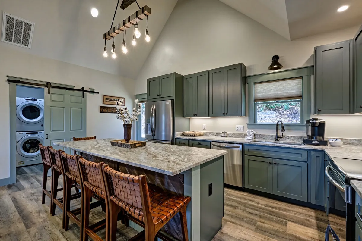 This image focuses on the kitchen island with bar stools, modern appliances, and a well-lit, welcoming atmosphere. The scene suggests family breakfasts, holiday dinners, and lively gatherings in a space designed for connection.