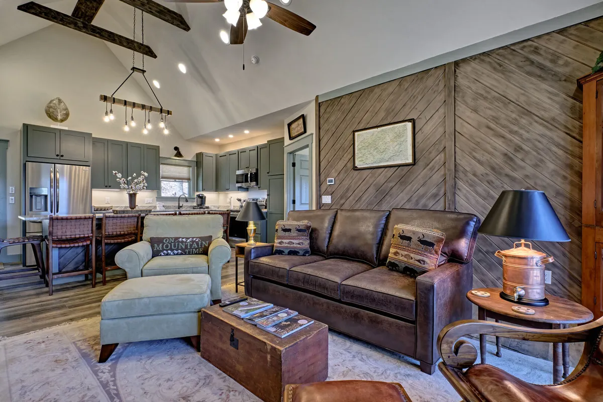A comfortable leather sofa, colorful accent chair, and rustic coffee table set the tone for relaxation and conversation. The kitchen area is visible in the background, highlighting the open-concept layout. The arrangement invites both casual lounging and social activities like board games or shared meals.